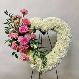 Heart-shaped white floral wreath with pink roses and carnations on a stand