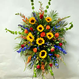 Tall standing floral spray with sunflowers, roses, and blue flowers