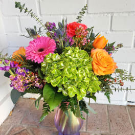 Colorful bouquet with hydrangea, gerbera daisy, roses, and tulips in a glass vase.