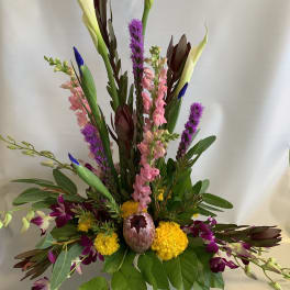 Tall mixed floral arrangement with calla lilies, orchids, and purple spikes