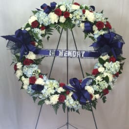 Heart-shaped funeral wreath with red, white, and blue flowers on an easel