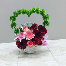 Basket arrangement with pink, red, and lavender flowers and a green heart handle
