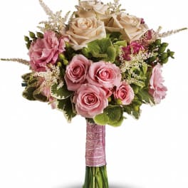 Bouquet of pink and cream roses with green accents and a pink wrapped handle