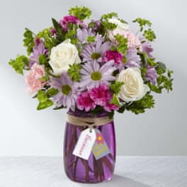 Bouquet of pink, lavender, and white flowers in a purple glass vase