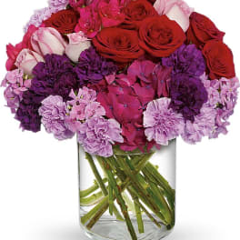 Bouquet of red roses, pink hydrangeas, and purple carnations in a clear glass vase