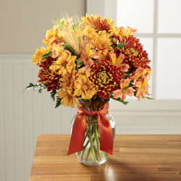 Bouquet of orange and yellow flowers in a glass vase with a red ribbon