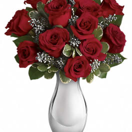 Red roses arranged in a clear glass vase with variegated greenery