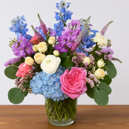 Mixed bouquet of blue, pink, and cream flowers in a clear glass vase
