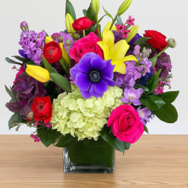 Colorful bouquet in a square glass vase with roses, lilies, and purple blooms
