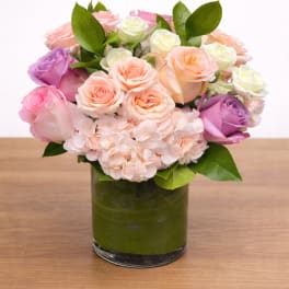 Pink, peach, and white roses arranged in a glass vase