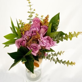 Tall bouquet of mauve roses and lavender mums with yellow filler in a clear glass vase