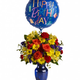 Bright birthday bouquet of orange roses and yellow daisies in a blue vase with a blue Happy Birthday balloon.