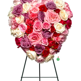 Heart-shaped arrangement of pink, red, lavender, and cream roses on a metal easel stand