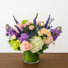 Bouquet of pink and cream roses with purple flowers in a green glass vase
