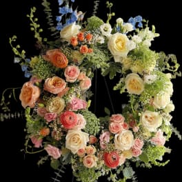 Large floral wreath with roses, ranunculus, and blue delphinium on a black background