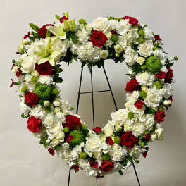 Heart-shaped floral wreath with red, white, and green flowers on a stand