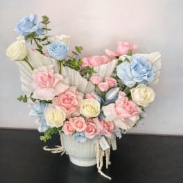 Pastel roses arranged in a white vase with pleated paper accents