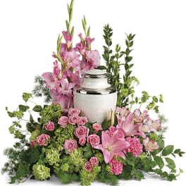 Pink floral arrangement around a white urn with silver trim