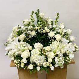 Large white floral arrangement with roses, lilies, and hydrangeas on a wooden stand