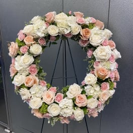 Large floral wreath of white, blush, and peach roses on a black stand