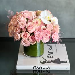 Low round pink rose arrangement with white orchid in a glass vase on a book