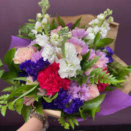 Mixed bouquet of pink, white, purple, and red flowers wrapped in purple paper