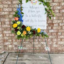 Standing floral tribute with butterflies and a memorial sign
