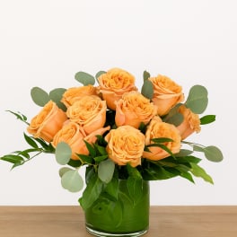 Orange roses in a green glass vase with eucalyptus