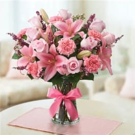 Pink lilies and roses arranged in a glass vase with a pink ribbon