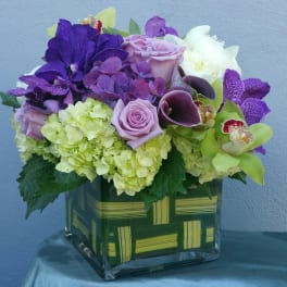 Purple and green floral arrangement in a square glass vase