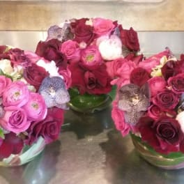 Three pink and burgundy rose arrangements in glass bowls