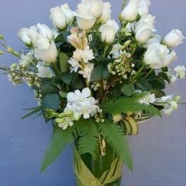 White roses and orchids arranged in a green glass vase