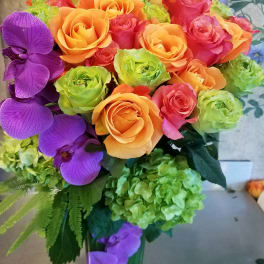 Bouquet of orange and pink roses with purple orchids in a glass vase