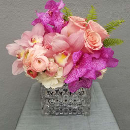 Pink roses and orchids arranged in a clear square vase