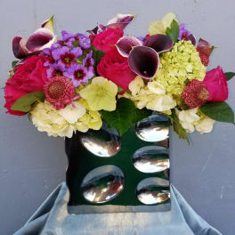 Mixed bouquet with pink roses, purple flowers, and calla lilies in a green vase