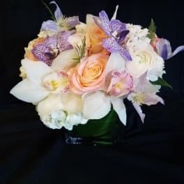 Pastel bouquet of roses, orchids, and white lilies in a glass vase