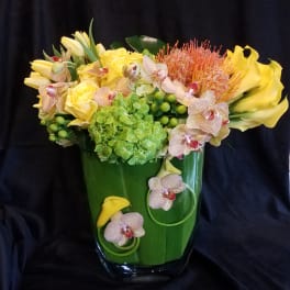 Yellow flowers and orchids arranged in a green glass vase