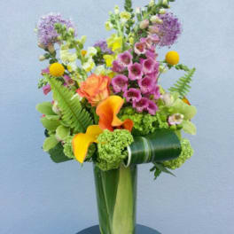 Colorful bouquet with orange calla lilies and purple blooms in a tall glass vase