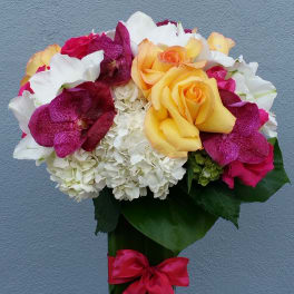 Bouquet of yellow roses, white hydrangeas, and magenta orchids in a glass vase
