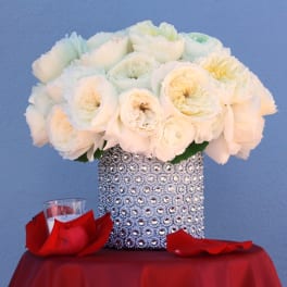 White rose bouquet in a rhinestone-covered vase with red petals nearby