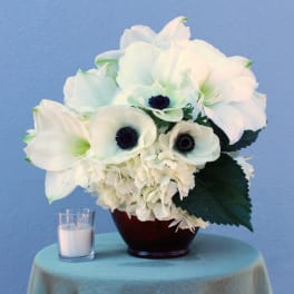 White floral arrangement in a dark vase beside a small candle