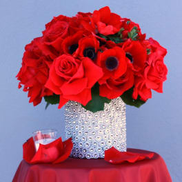 Red rose bouquet in a silver textured vase with red petals on a table
