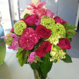 Pink and red flower bouquet in a clear glass vase with a ribbon