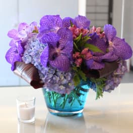 Purple orchid and hydrangea arrangement in a blue glass vase