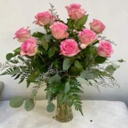 Pink roses arranged in a clear glass vase with greenery
