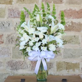 White floral arrangement in a glass vase with a white ribbon