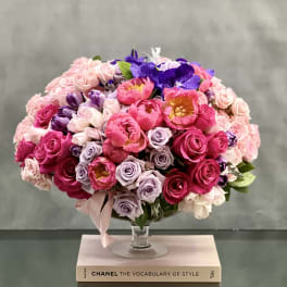 Round bouquet of pink, lavender, and purple flowers in a glass vase.