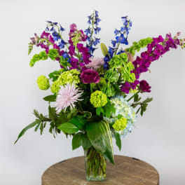 Tall mixed bouquet in a clear glass vase with blue, purple, and green flowers