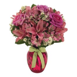 Pink roses and lilies in a red glass vase with a green ribbon