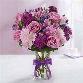 Pink and purple bouquet of roses and daisies in a glass vase with a purple ribbon